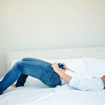 Woman on bed struggling to button jeans