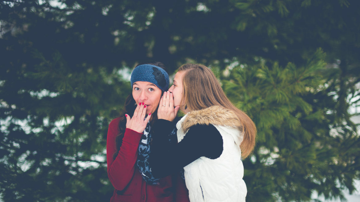 Woman whispering on another woman's ear