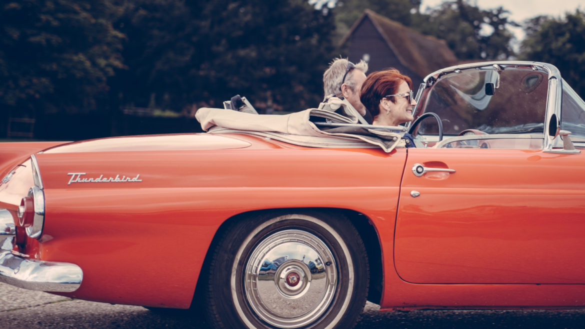 Mature man driving woman in classic covertible Thunderbird.