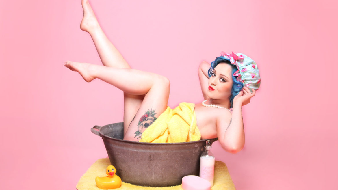 Woman laying in metal washtub with soap, sponge and rubber duck.
