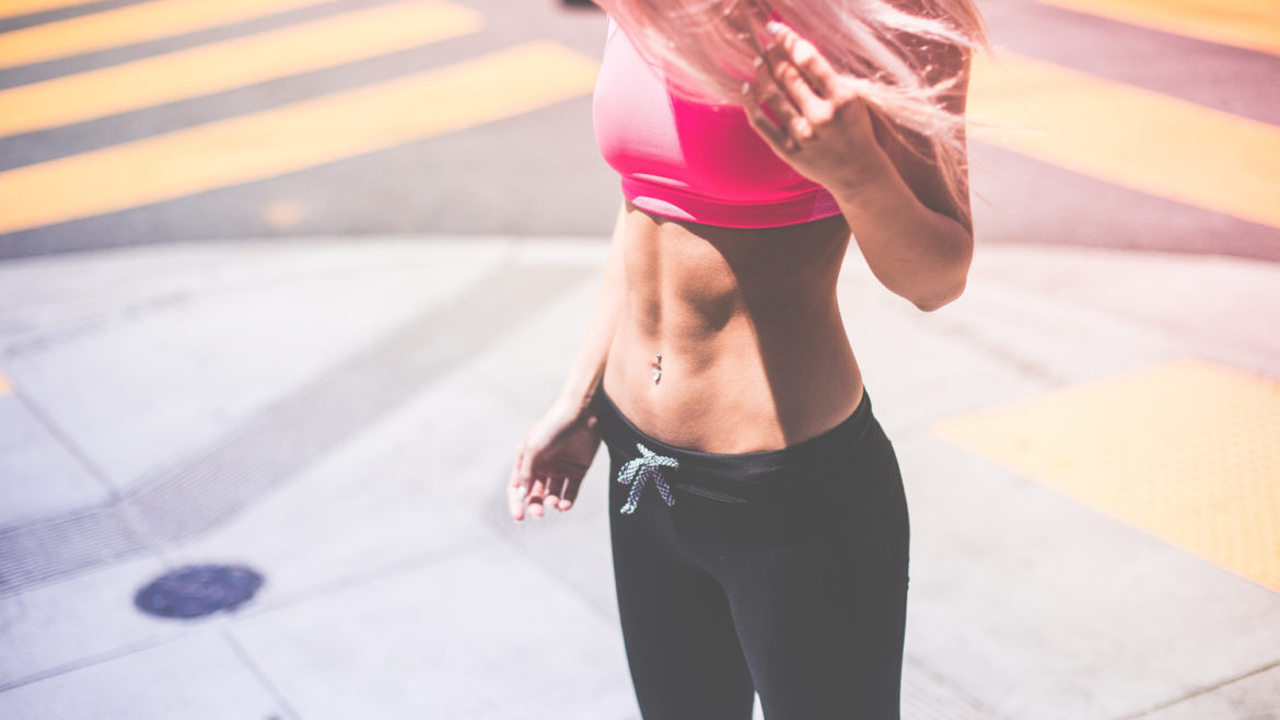 Woman standing on street corner looking down at her abs.