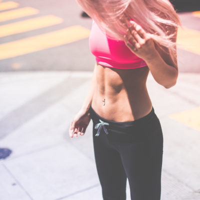 Woman standing on street corner looking down at her abs.