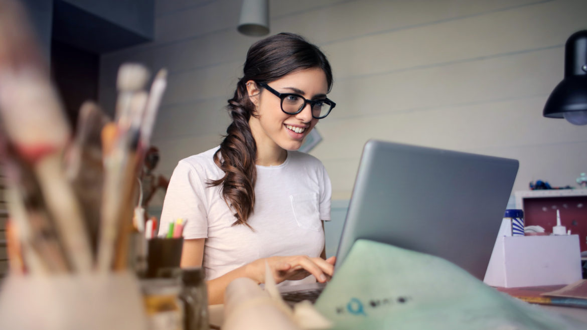 Woman with ponytail and glasses using her laptop.