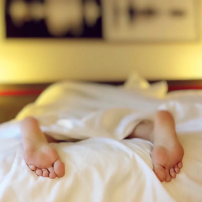 Person lying in bed face down under a white blanket with their feet sticking out.