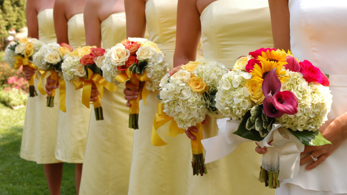 Women wearing white and yellow strapless dresses holding white, red and yellow bouquets.