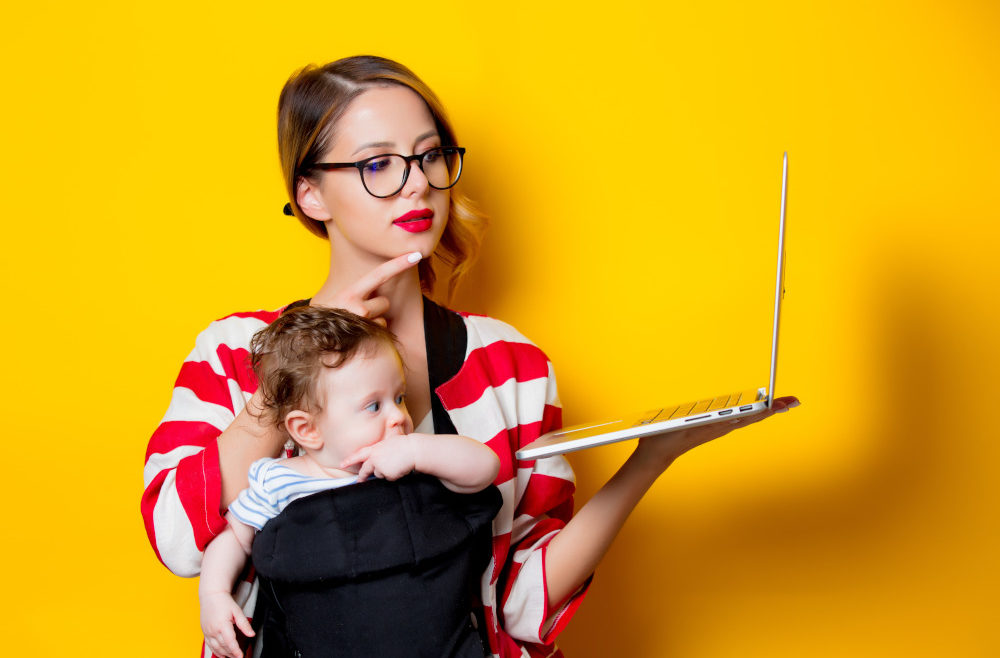 little baby in carrier and mother with laptop computer on yellow background.
