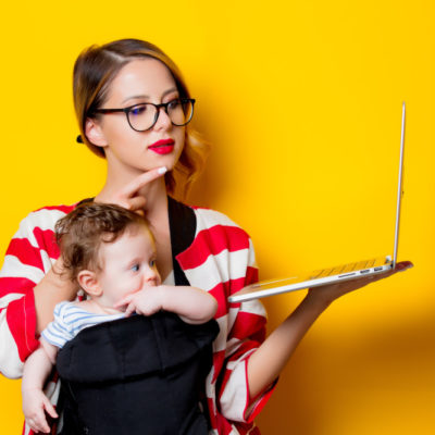 little baby in carrier and mother with laptop computer on yellow background.