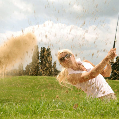 Woman playing golf hitting a ball out of a sand dune.