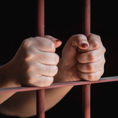 Woman's hands holding on to jail cell bars.