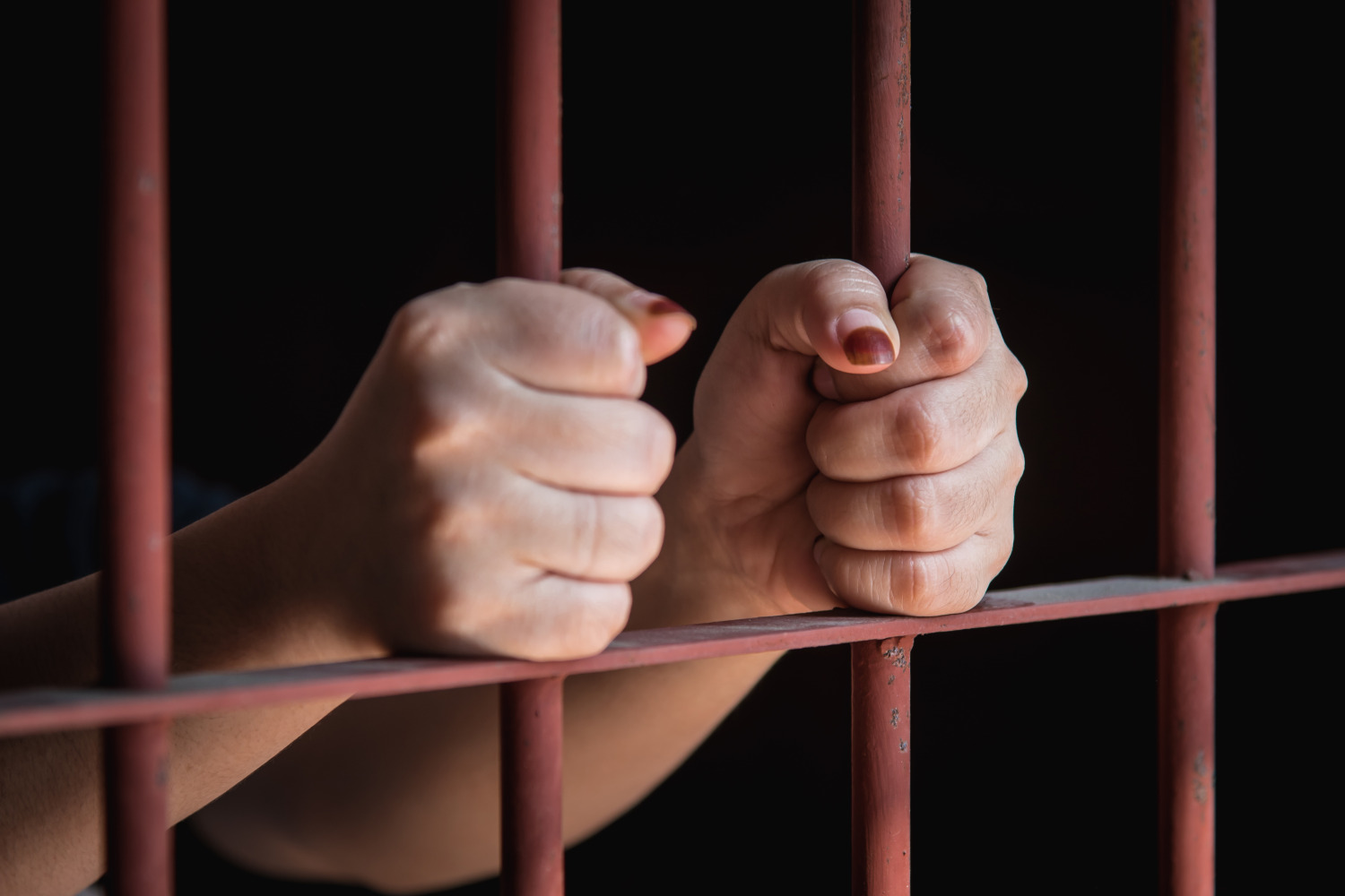 Woman's hands holding on to jail cell bars.