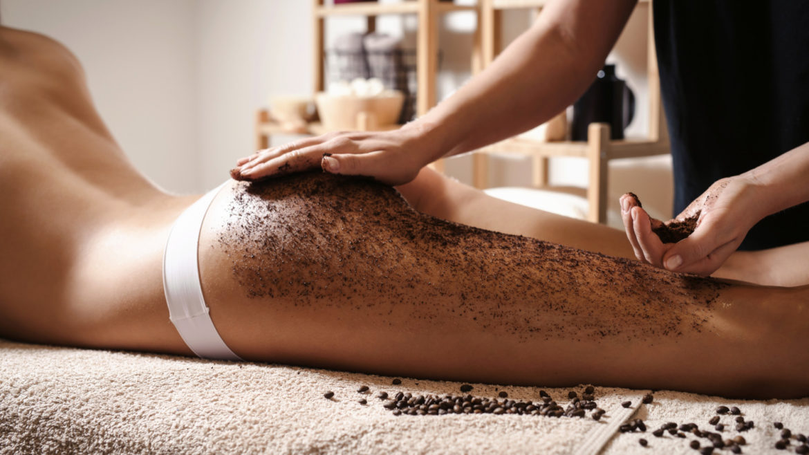 Close up of woman getting buttocks and legs massage with coffee scrub at spa.