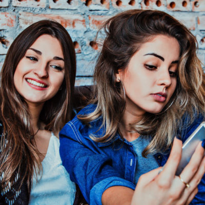 2 women posing while holding a cellphone up to take a selfie.