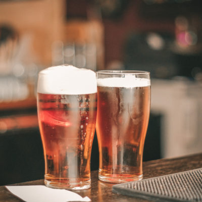 Upclose image of 2 pilsner glasses on a bar counter filled with beer.