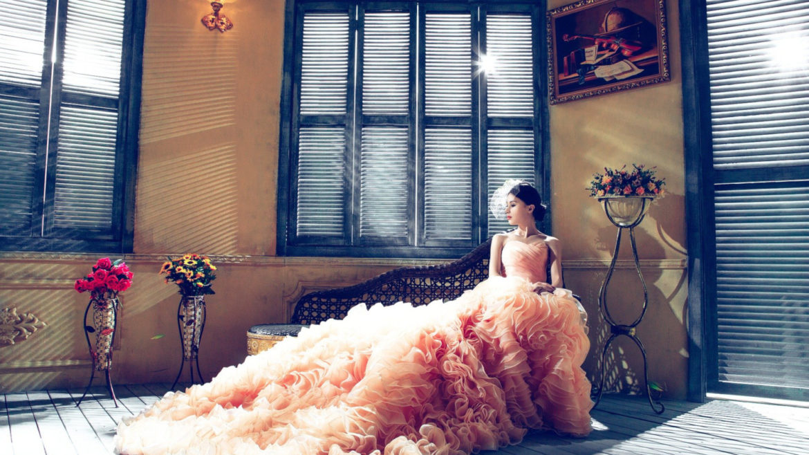 Bride wearing a blush colored wedding dress with a long textured train.