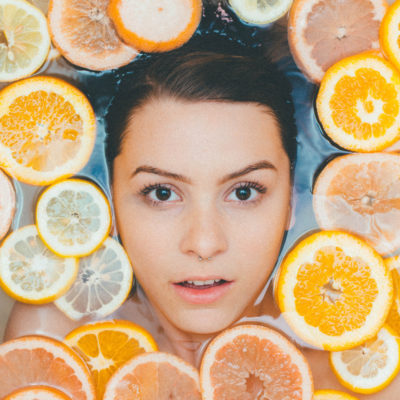 Woman's face surrounded by sliced lemons floating in water.
