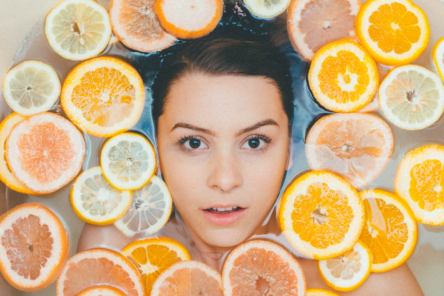 Woman's face surrounded by sliced lemons floating in water.