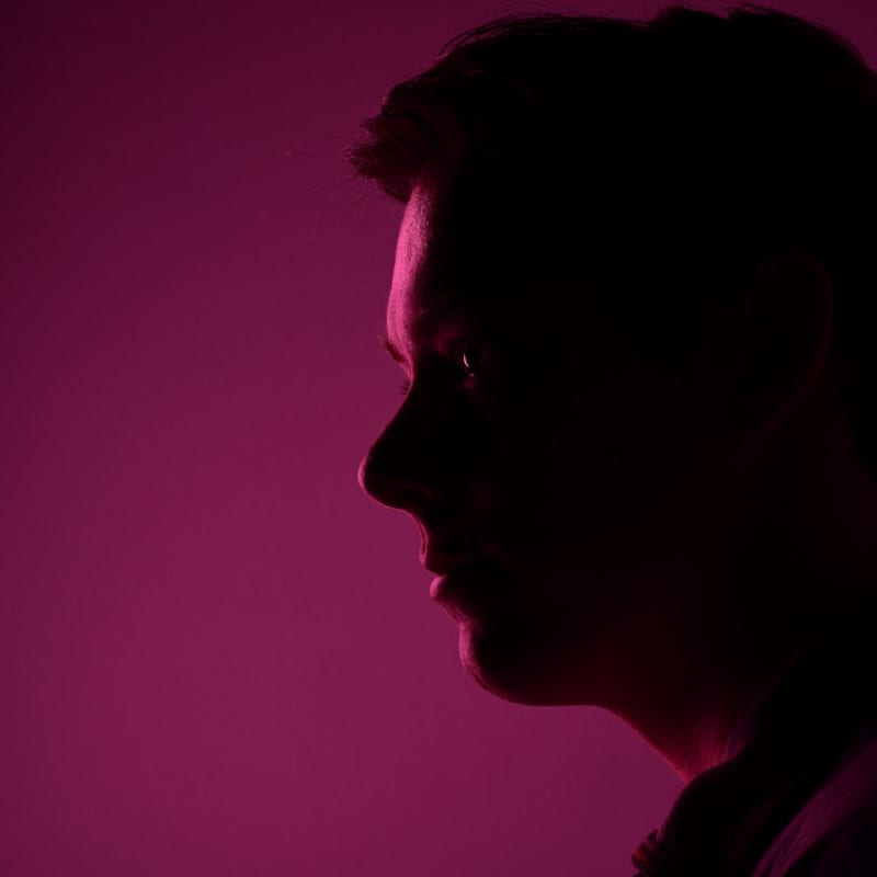 Woman facing left side in a shaded purple light.
