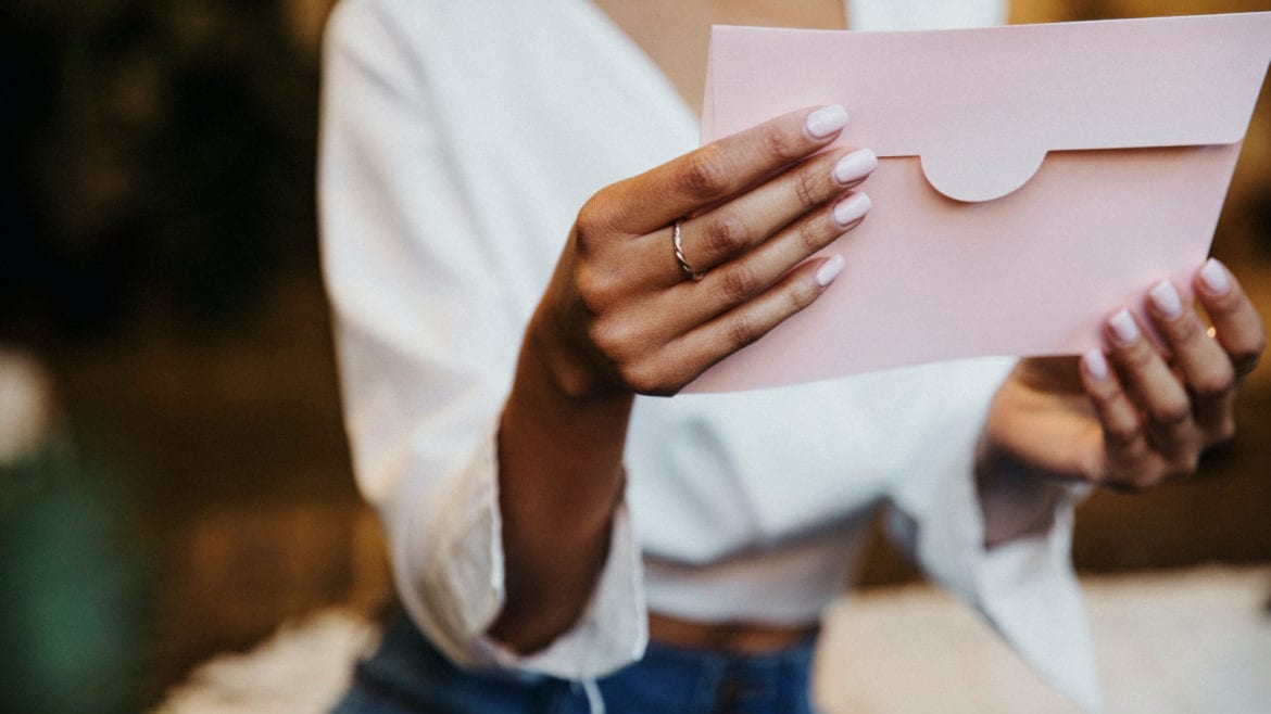 Gifting plastic surgery concept. Woman with pink nails looking at a pink card envelope.