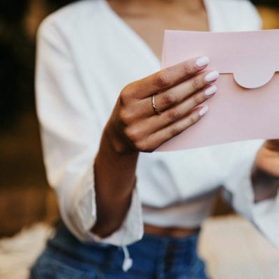 Gifting plastic surgery concept. Woman with pink nails looking at a pink card envelope.